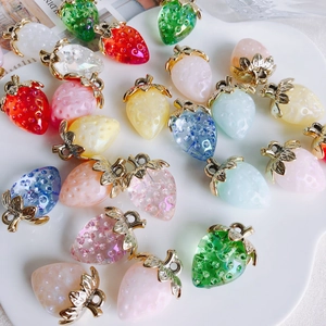 Colorful resin strawberry pendants with gold metal leaves in a white ceramic dish