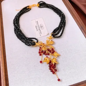 Close-up of vintage multilayer black beaded necklace with red grape leaf pendant