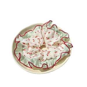 Floral cherry print scrunchie with red bow and lace trim in a beige ceramic dish