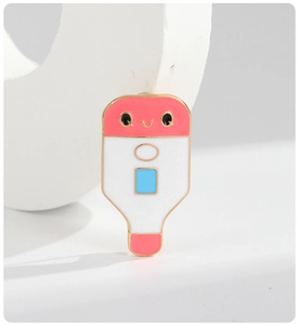Detail of pink cartoon thermometer brooch with gold metal edges and glossy enamel finish