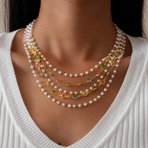 Detail of a multi-layer gold necklace with white pearls and colorful gemstones on a model