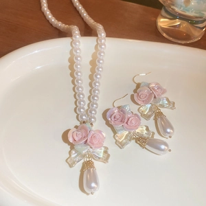 Floral jewelry set with pink rose and teardrop pearls on white ceramic tray