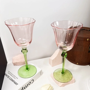 Detail of two vintage pink flower wine glasses with green bamboo stems on a wooden table