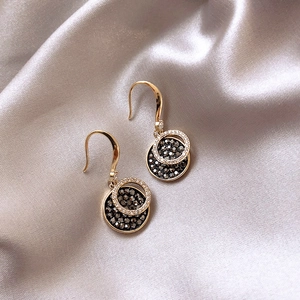 Detailed close-up of gold disc earrings featuring black stones and white crystals on silk