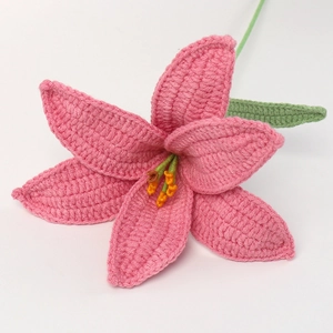 Close-up of a handmade pink crochet lily flower with detailed knitted textures and green leaves