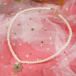 Detailed view of pearl necklace with green snowflake pendant and red gemstone charm
