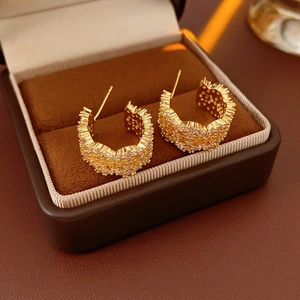 Close-up of gold C-shaped earrings with zircon inlay in a brown jewelry box