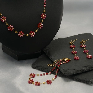 Floral jewelry set featuring red faceted beads and gold-tone beads on grey slate