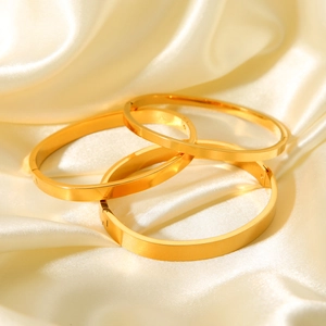Detailed macro view of three polished gold titanium steel bangles on silk fabric background