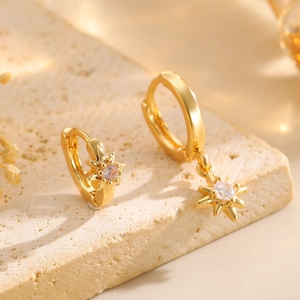 Macro shot of gold-plated star earrings with clear cubic zirconia on stone background