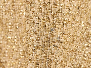 Dettaglio macro del tessuto tweed dorato con fili metallici e texture di paillettes