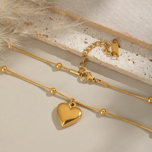 Détail du collier pendentif cœur doré avec chaîne à billes sur une surface en pierre