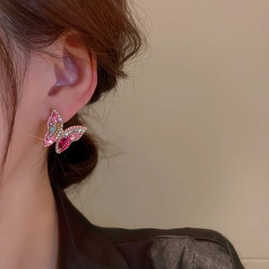 Macro side view of a model wearing sparkling pink and green butterfly stud earrings