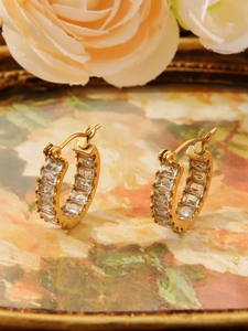 Close-up of gold plated C-shape earrings with cubic zirconia on a vintage floral plate