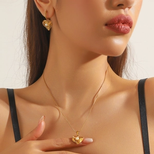 Close-up of gold-plated heart necklace and earrings set with central pearl detail