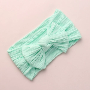 Detailed view of mint green cable knit baby headband with a large decorative soft bow