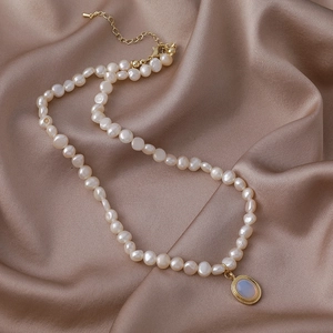 Detalle de collar de perlas con colgante de ópalo azul sobre una tela de satén