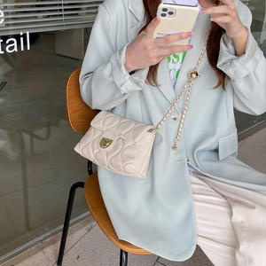 Beige quilted chain crossbody bag with gold-tone metal twist lock on a fashion model