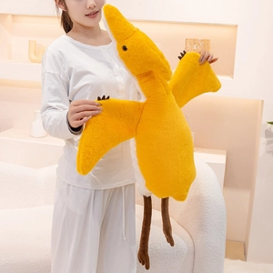 Soft yellow pterosaur plush dinosaur toy pillow held by person in cozy home setting