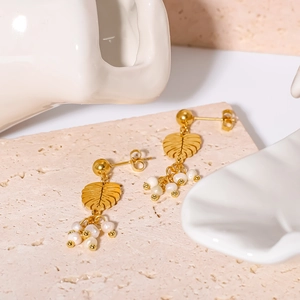 18K gold-plated leaf earrings with natural white pearls on a textured travertine stone