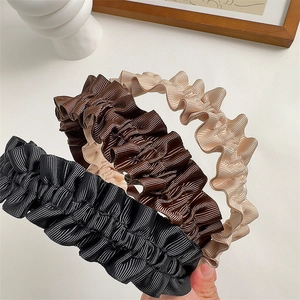 Close-up of pleated wide headbands in black, brown, and beige with soft satin texture