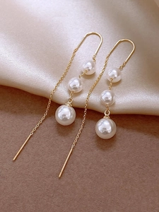Macro view of gold chain drop earrings with three elegant white pearls on silk
