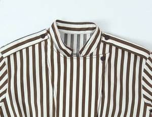 Dettaglio camicia a righe con collo alla coreana, abbottonatura sfalsata e mostrine sulle spalle