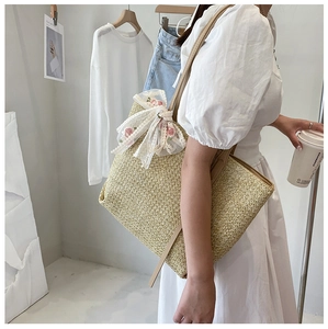 Detail of straw woven tote bag featuring a delicate white floral lace bow charm