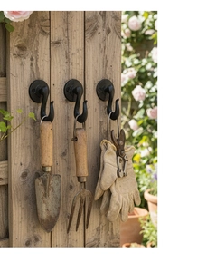 Three vintage black cast iron garden hooks mounted on wood fence holding tools