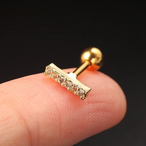 Close-up of a gold T-shaped zircon stud earring with a screw ball back on a fingertip