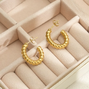 Detail of 18k gold plated stainless steel twisted hoop earrings on beige velvet tray