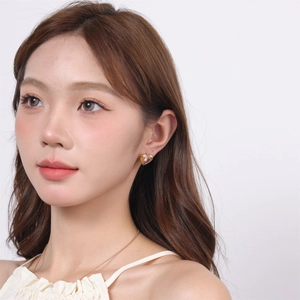 Close-up of a gold heart earring with pink gemstone on model ear with soft lighting