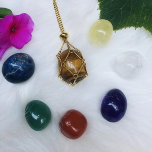 Tiger's eye stone in golden mesh net pendant on white plush background with crystals