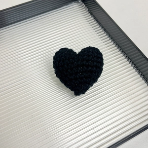 Close-up of a handmade black knitted heart brooch crafted from premium wool yarn