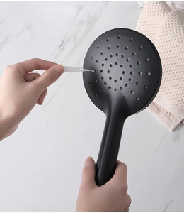 Macro detail of a mini cleaning brush unclogging holes on a black handheld shower head