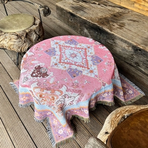Pink bohemian woven camping blanket with tassels and geometric patterns on a wooden deck