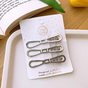 Close-up of three silver hollow geometric hair clips on a premium white display card