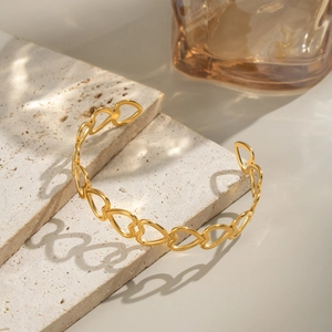 Macro detail of gold-plated heart-shaped hollow bangle on a textured travertine stone