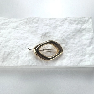 Minimalist golden geometric oval metal hair clip on textured white paper background