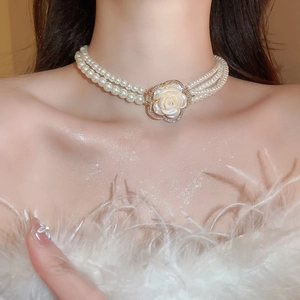 Close-up of three-row pearl necklace featuring a diamond-encrusted flower pendant on a model