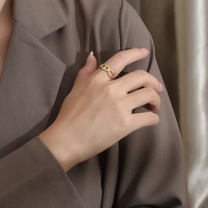 Close-up of a gold-plated C-shape anchor chain ring worn by a model in a minimal setting