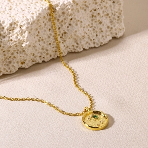 Detailed close-up of 18K gold zodiac pendant with green gemstone and small diamonds