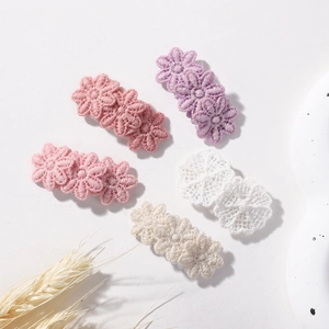 Detail of five handmade crochet flower hair clips in soft pastel colors on a beige background