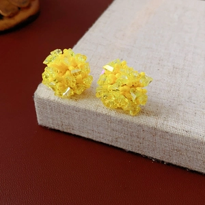 Close-up of yellow crystal bead cluster earrings on a beige display with leather background