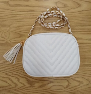 Dettaglio borsa bianca trapuntata a V in similpelle con catena dorata e nappa decorativa