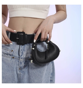 Detail of a black crescent waist bag with gold hardware worn on a wide leather belt