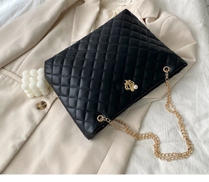 Detail of black quilted tote bag with gold crown charm on beige blazer background