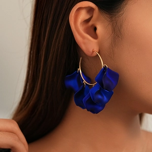 Close-up of matte dark blue petal charms hanging from a golden metal hoop earring