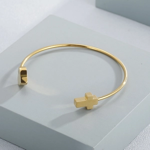 Detail view of gold open cuff bracelet with heart and cross charms on geometric display