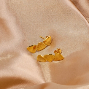 Macro detail of golden triangle earrings with lava texture on champagne silk fabric